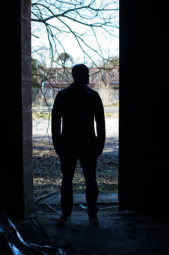 Silhouette of a man standing in the doorway of a derelict building