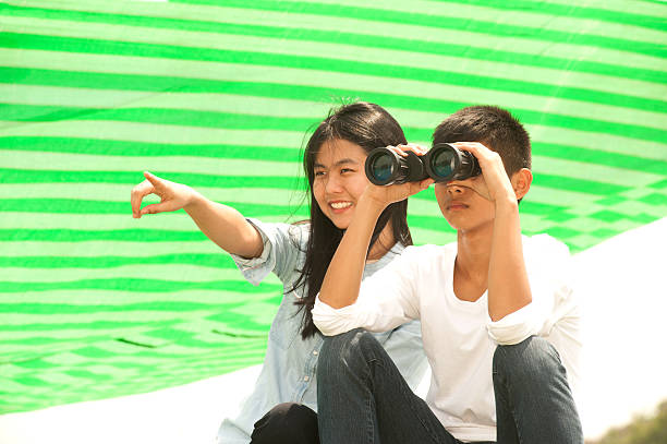 istock Young boy and girl sit on mound seeking Binoculars . 520556560