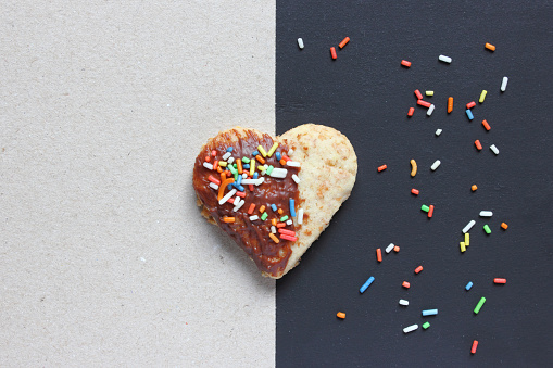 Heart shaped xmas cookie on black and white contrasting background with colorful sugar sprinkles - space for text