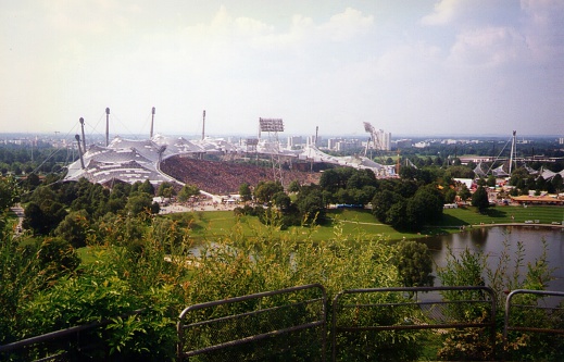 Munich, Germany - August 17, 1997: The Olympiapark view from Olympic mountain, built for the 1972 Summer Olympics. The Park continues to serve as a venue for cultural, social, and religious events. In the background, the Olympic Stadium, crowded with soccer funs looking the football match.