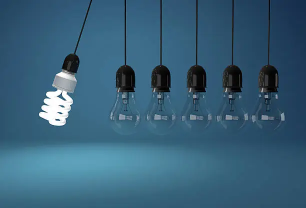 Energy saving bulb and incandescent bulb in perpetual motion over blue background