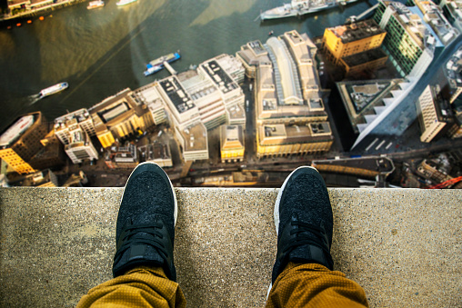Two feet at the edge of a rooftop of a high building. Buildings and a river in the background.