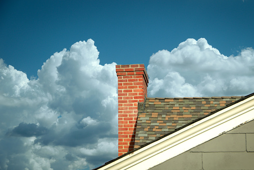 Part of tiled roof with brick chimney against clouds