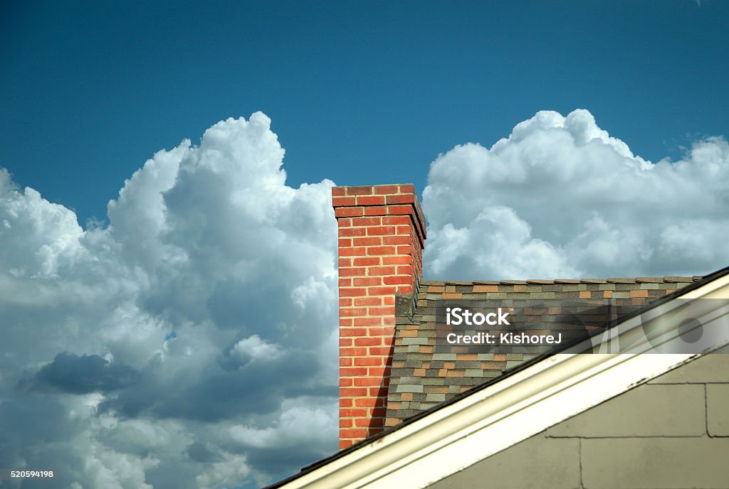 Part of tiled roof with brick chimney against clouds Part of tiled roof with brick chimney against blue sky with beautiful cloud formations and diagonal composition Chimney Stock Photo