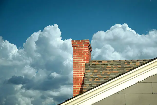 Photo of Part of tiled roof with brick chimney against clouds
