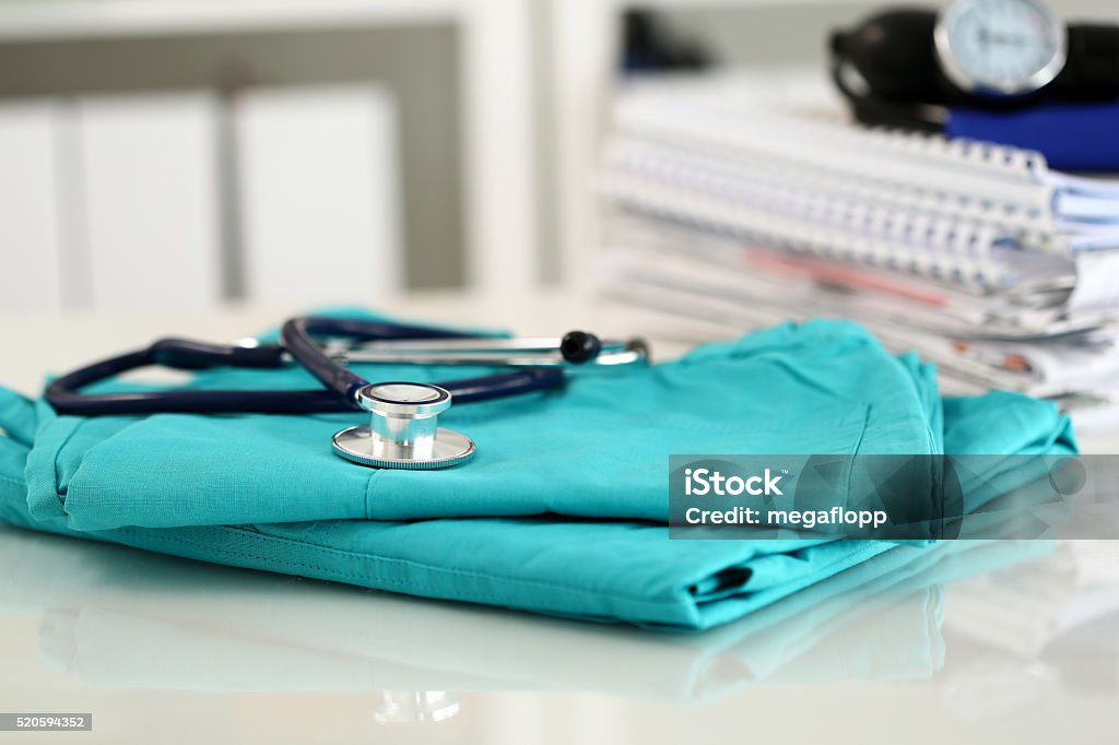 Medical stethoscope lying on green doctor uniform closeup Medical stethoscope lying on green doctor uniform closeup. Medical tools and instruments shop, therapeutist workspace, physical, patient examination, blood pressure measurement concept Assistance Stock Photo