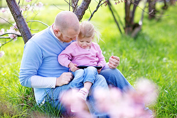 istock Father and daughter using tablet device in cherry blossom garden 520594948