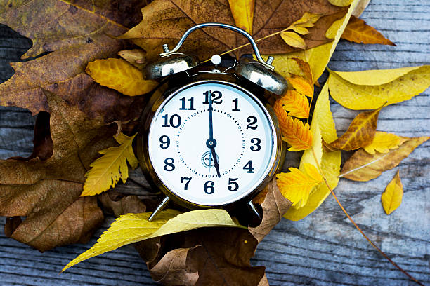 istock Retro clock on a wooden table with autumn leaves 520601713