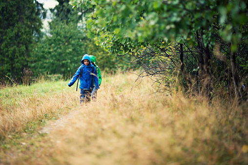 Two brave little boys caugh by the rain on the trail. The kids are wearing backpacks, waterproof jackets and hoods.