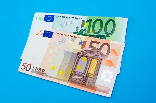 High angle view of fifty and one hundred euro banknotes. Horizontal composition. There is 50 (fifty) euro banknote top of 100 (one hundred) euro banknote over blue background. Studio shot. Developed from RAW format.