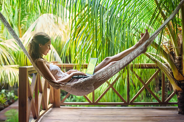 giovane donna distesa in un amaca con computer portatile - summer vacations women hammock foto e immagini stock