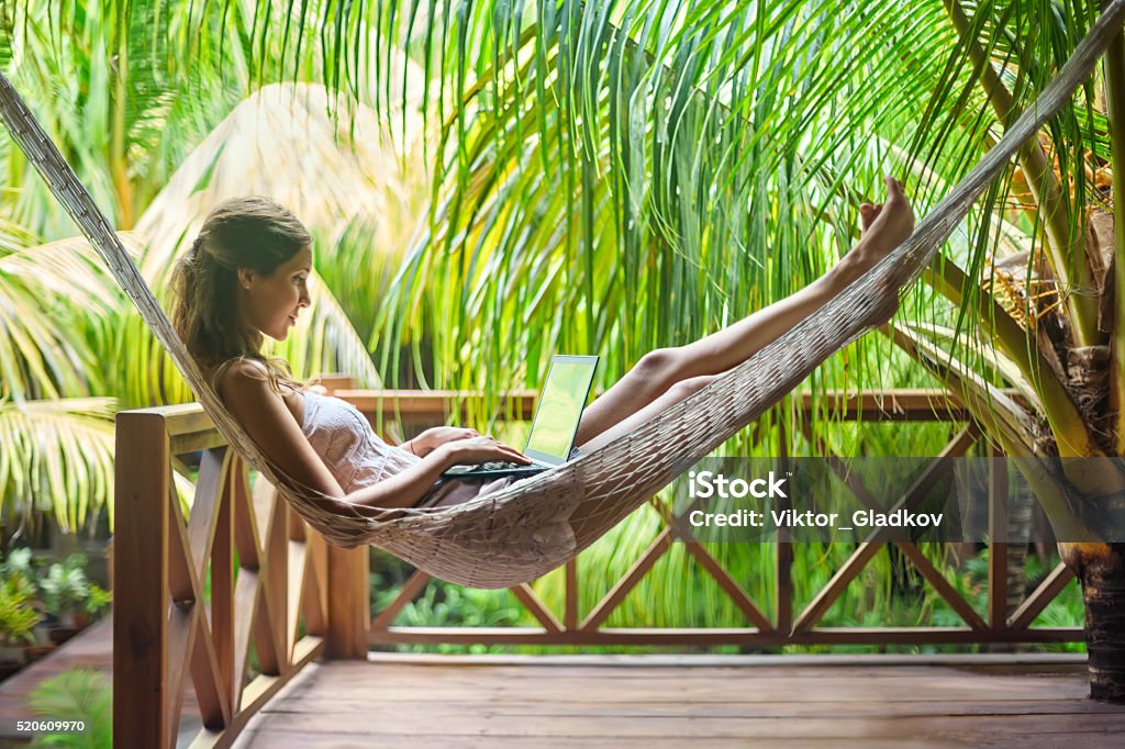 Young woman lying in a hammock with laptop Young beautiful woman lying in a hammock with laptop in a tropical resort Working Stock Photo