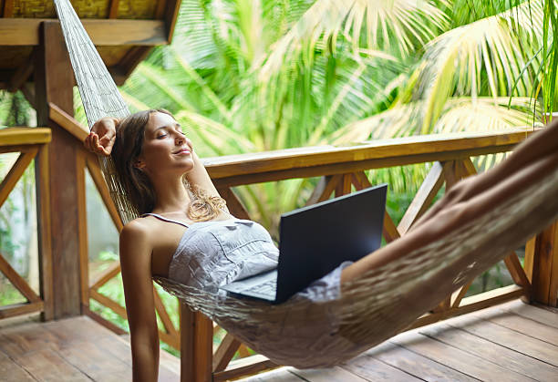 Young woman relaxing in hammock with laptop in tropical resort stock photo