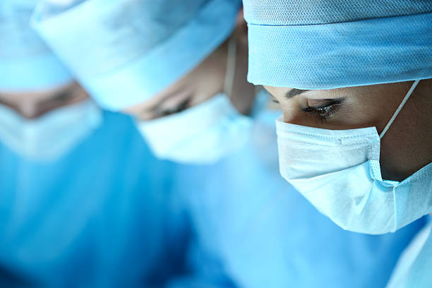 tre chirurghi al lavoro che operano in teatro chirurgica - medical supplies scalpel surgery equipment foto e immagini stock