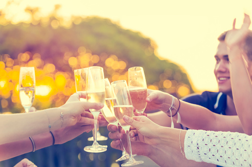 Group of friends drinking champagne. They are having a dinner party at sunset and are toasting. They are outdoors and look happy and smiling.
