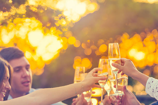 Group of friends drinking champagne. They are having a dinner party at sunset with the sun in the background. They are outdoors