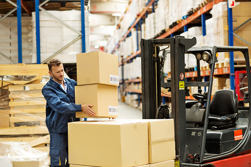 Male worker loading cardboard boxes on forklift at distribution warehouse