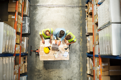 High angle view of supervisor using laptop with workers at distribution warehouse
