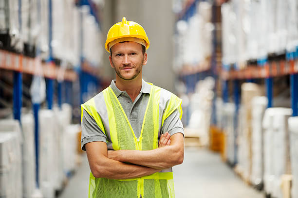 confident worker standing in warehouse - 헬멧 뉴스 사진 이미지