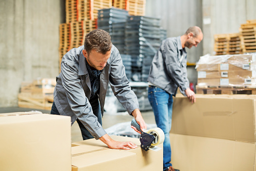 Male workers packing cardboard boxes at distribution warehouse