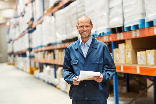 Portrait of happy worker standing by shelves in distribution warehouse