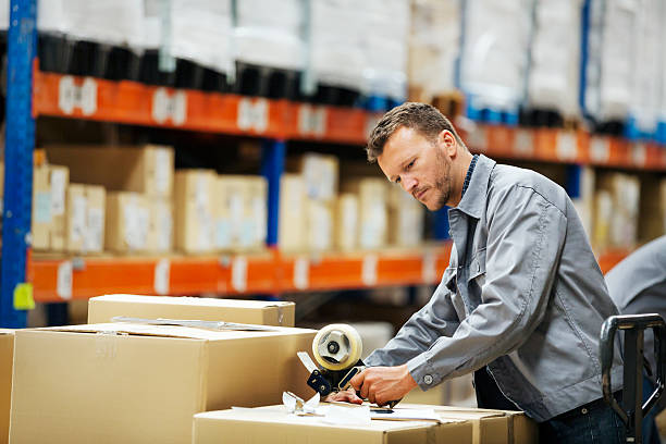 Worker packing cardboard box in warehouse Male worker packing cardboard box at distribution warehouse packing stock pictures, royalty-free photos & images