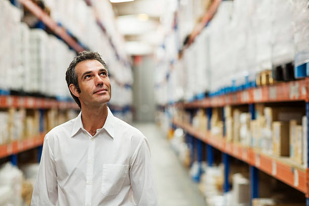 Supervisor in warehouse Smiling supervisor looking at stock arranged on shelves in warehouse looking up stock pictures, royalty-free photos & images
