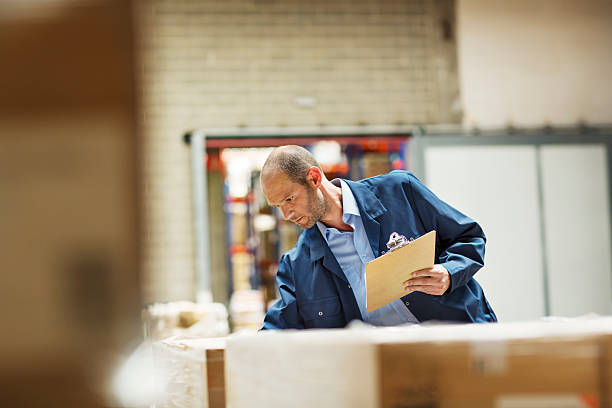 Worker examining stock in warehouse Worker examining stock while holding clipboard in distribution warehouse 2655 stock pictures, royalty-free photos & images
