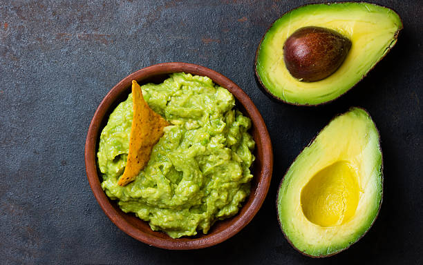 Latin American sauce guacamole and avocado sandwiches on dark background. Traditional latinamerican mexican sauce guacamole in clay bowl and avocado sandwiches on dark background. Top view guacamole stock pictures, royalty-free photos & images