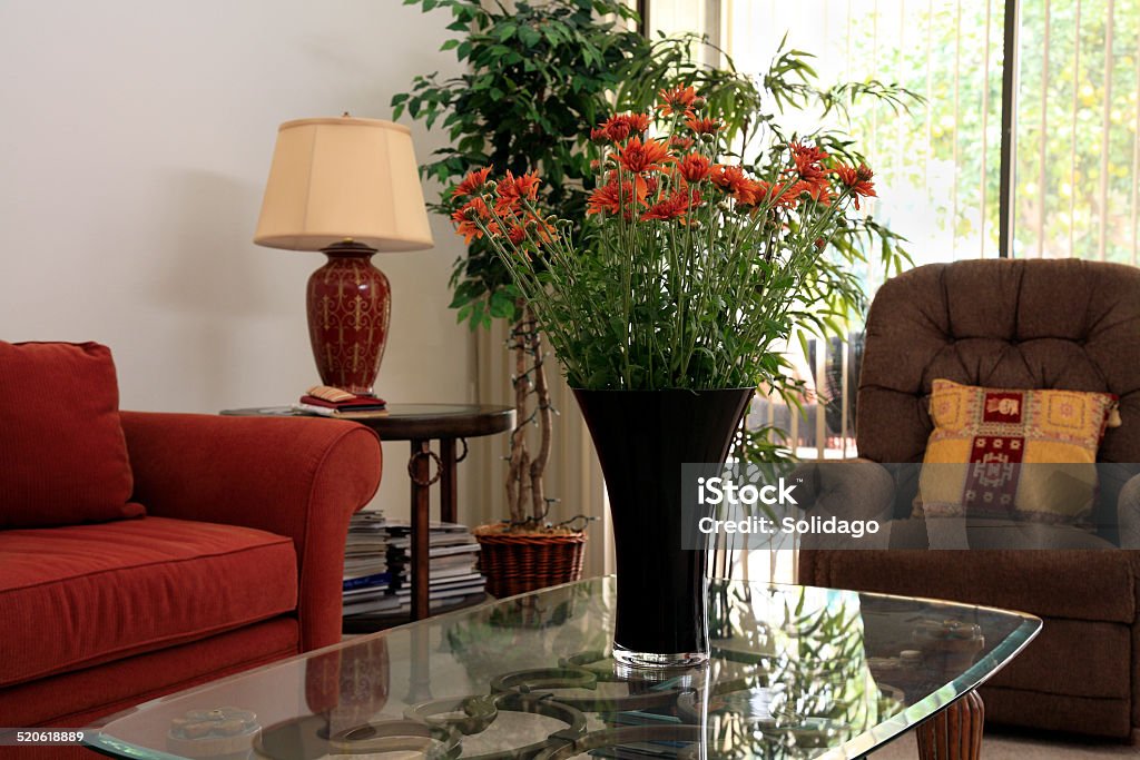 Comfortable Corner In The Living Room Recliner chair with edge of sofa, glass coffee table,and vase of flowers. Lots of books.  Natural light. No People Stock Photo