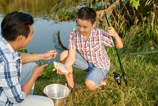 Preteen Vietnamese boy enjoying fishing with his father