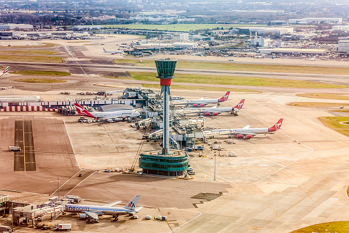 London, England, UK - 20th February, 2012: An elevated view of the Air Traffic Control Tower near Terminal Three at London Heathrow Airport. Aeroplanes from Virgin Atlantic, Qantas and American Airlines are parked at gates at the terminal.