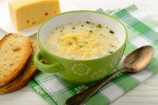 Potato soup with cheese on white wooden table.