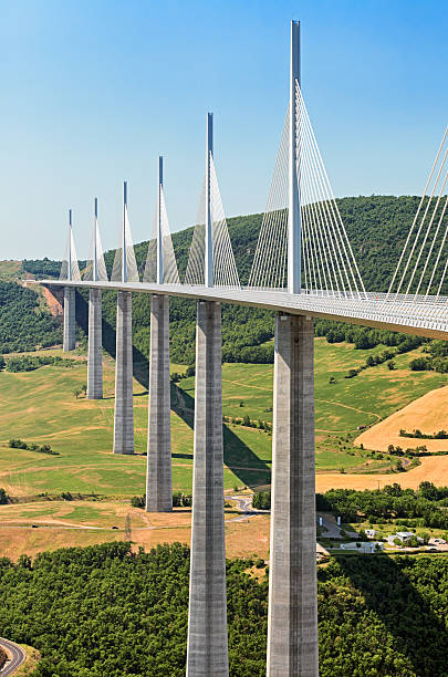 Millau, Aveyron, France - August 08, 2006: Panoramic view of the Millau Viaduct suspension bridge , co-designed by Norman Foster, set in a green summer landscape of rolling hills and crossing the River Tarn on which sails a single canoe.