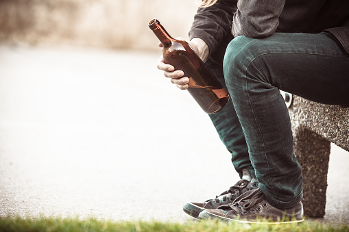 Hombre deprimido con botella de vino sentado sobre banco al aire libre photo