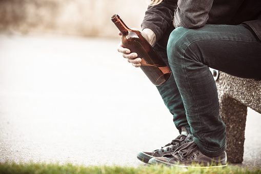 Man depressed with wine bottle sitting on bench outdoor. People abuse and alcoholism problems.