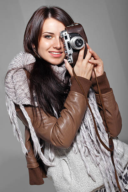 Dark haired attractive woman with analog camera in woolen scarf indoors, isolated on grey background. 