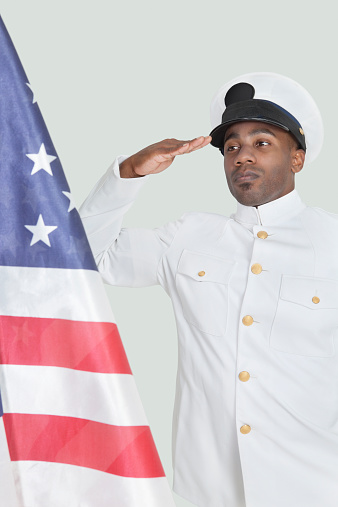 Young Navy officer saluting at American flag against gray background