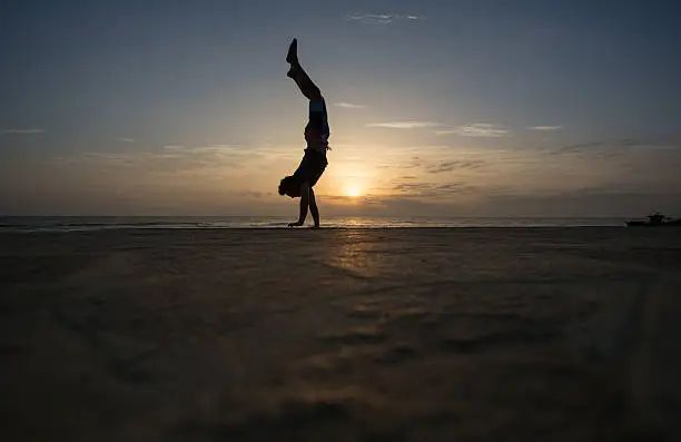 Photo of silhouetted man doing handstand in sunset