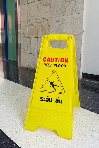 Caution wet floor orange fold out sign without text in a bright corridor, closeup detail Slipping man symbol, object up close, nobody, copy space Accidents, at work, cleaning services abstract concept