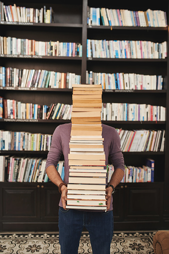 Man carrying big stack of books in library