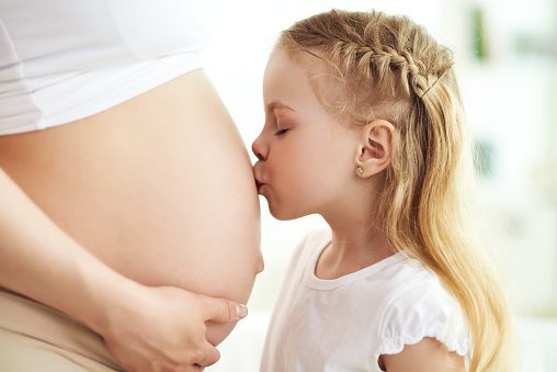 Little girl kissing her pregnant mothers belly