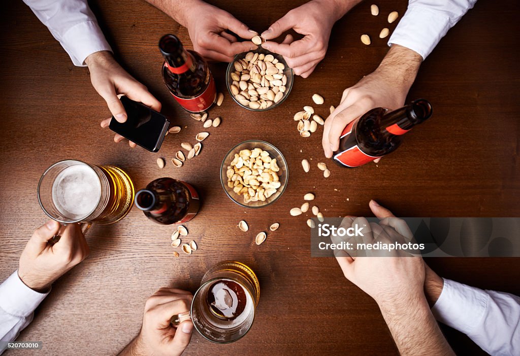 Just bromance? Four male friends drinking beer in pub, two of them unexpectedly holding hands Adult Stock Photo