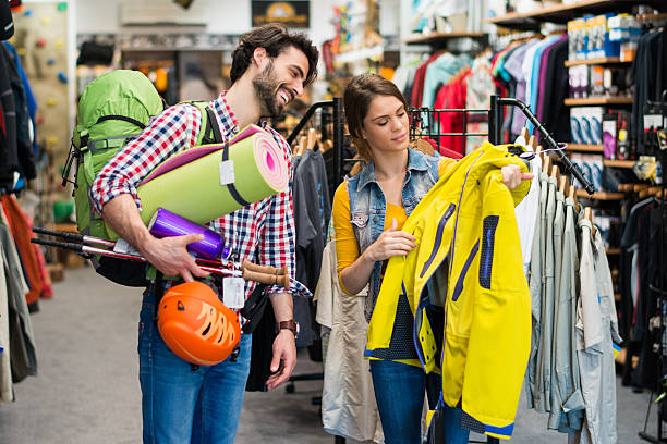 Man looking to buy jacket and outdoor equipment Man in sports store picking some hiking equipment, and asking a sales person about yellow jacket. sports equipment stock pictures, royalty-free photos & images
