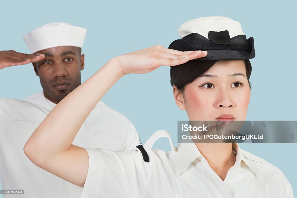 Solid portrait Confident female Navy officer and sailor saluting over light blue background 20-24 Years Stock Photo