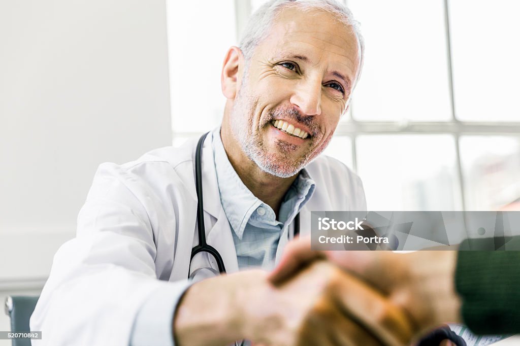 Confident doctor shaking hands with patient A photo of confident male doctor shaking hands with patient. Smiling mature medical professional is in clinic. Man is consulting healthcare practitioner in office. Doctor Stock Photo