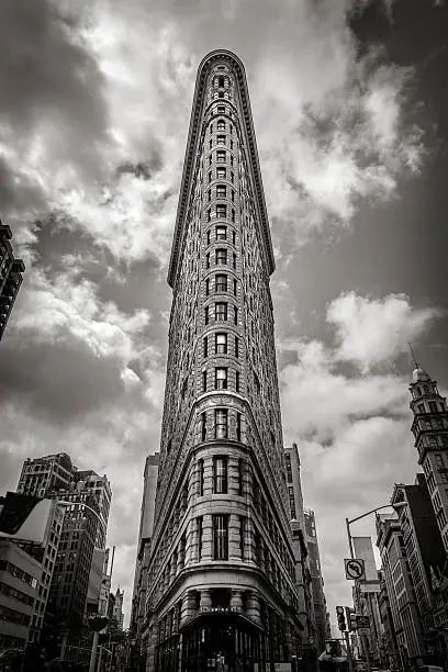 Vertical New York - The Flatiron Building stands right in the heart of Manhattan, at the intersection of two famous NYC landmarks: 5th Avenue and Broadway. It was completed in 1902 and was one of the first skyscrapers in New York City. Its name comes from its highly recognizable triangular shape and the neighborhood around it was named after it and is known as the Flatiron District. Black & White New York beaux-art architecture