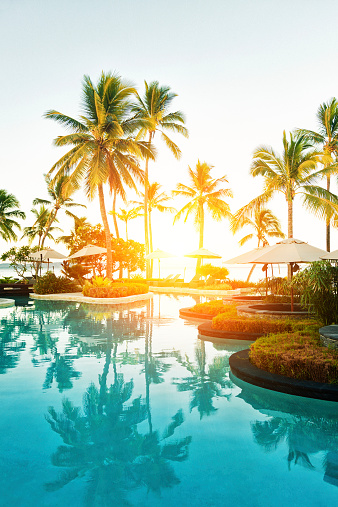 Outdoor pool area at a tropical resort during sunset.