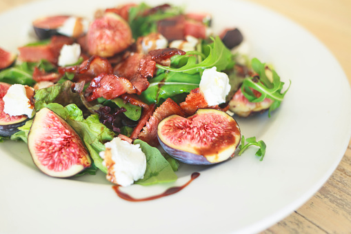 Healthy salad with arugula, goata cheese, fresh figs and bacon. Close up.