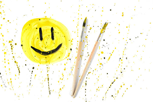 istock Closeup smiley symbol with paint brushes on yellow spray background 520740258